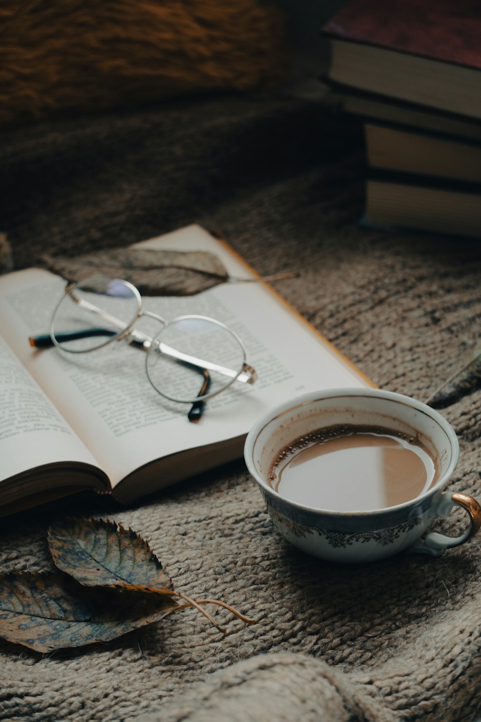 Offenes Buch, Brille und Kaffee auf einer gestrickten Decke.