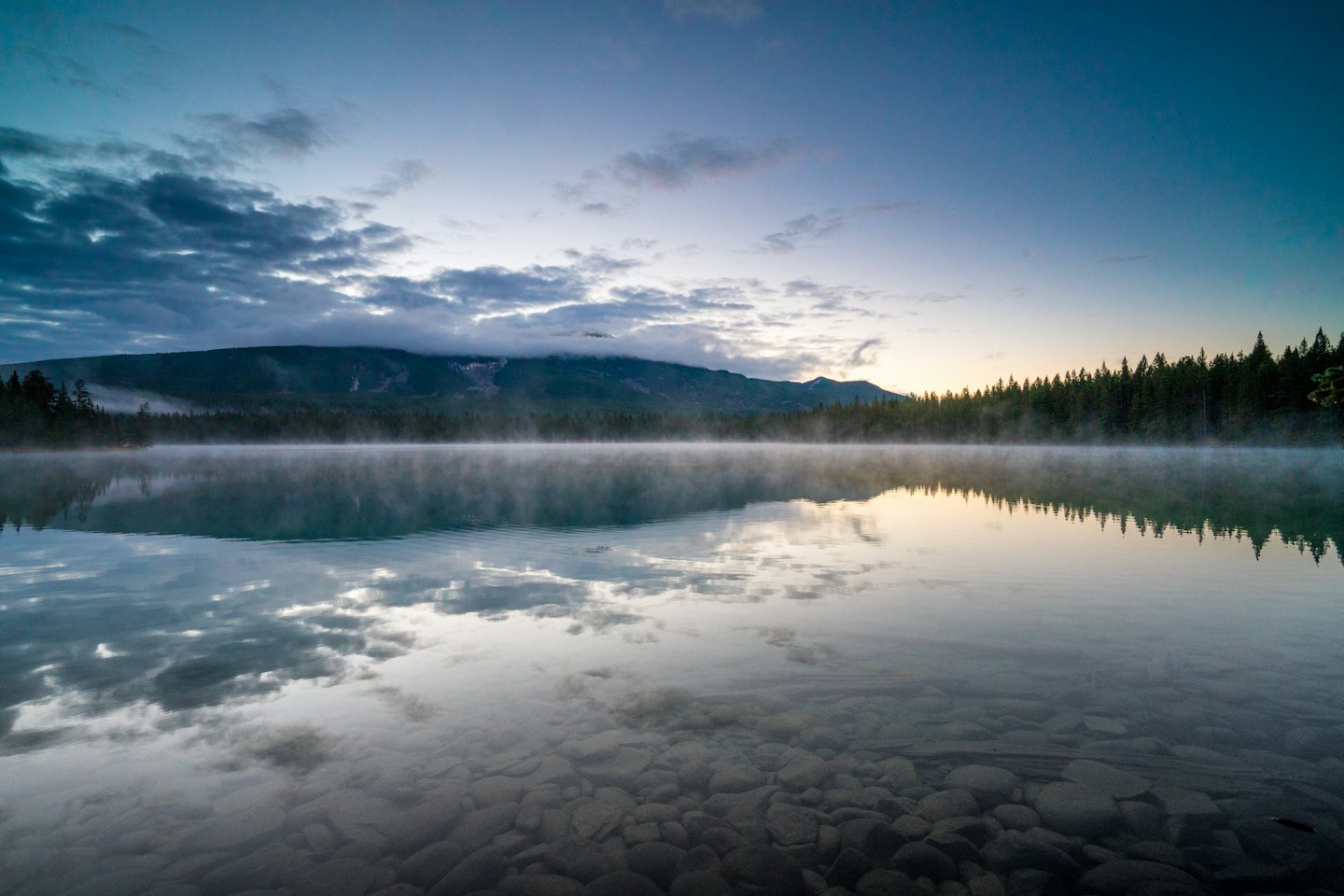 Nebeliger Bergsee im Morgengrauen mit Spiegelung des Waldes.