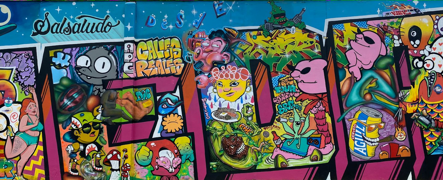 Bunte Graffiti-Wand mit Zeichentrickfiguren und verschiedenen Lebensmitteln.