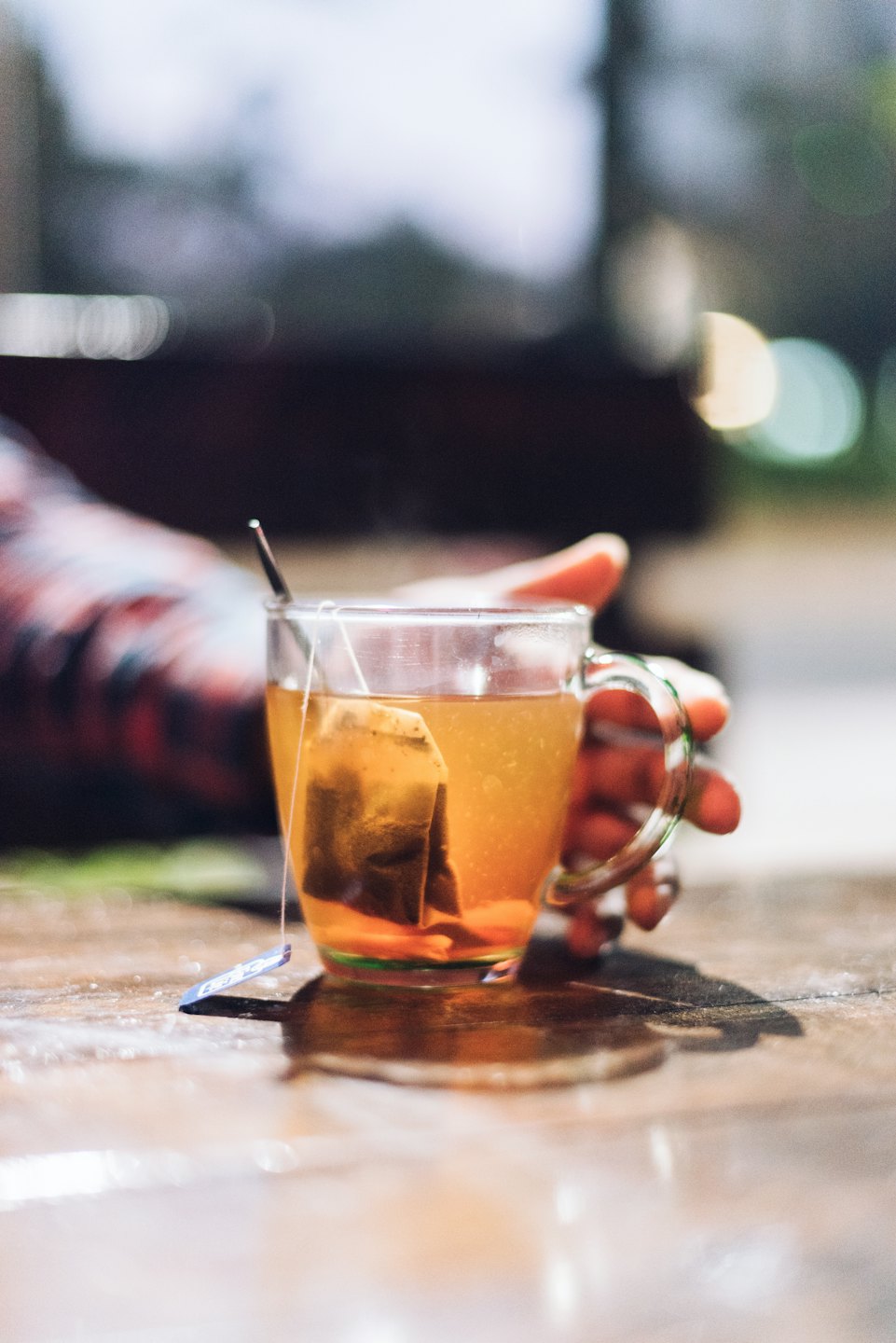 Hand hält eine Tasse Tee mit Teebeutel auf einem Holztisch.